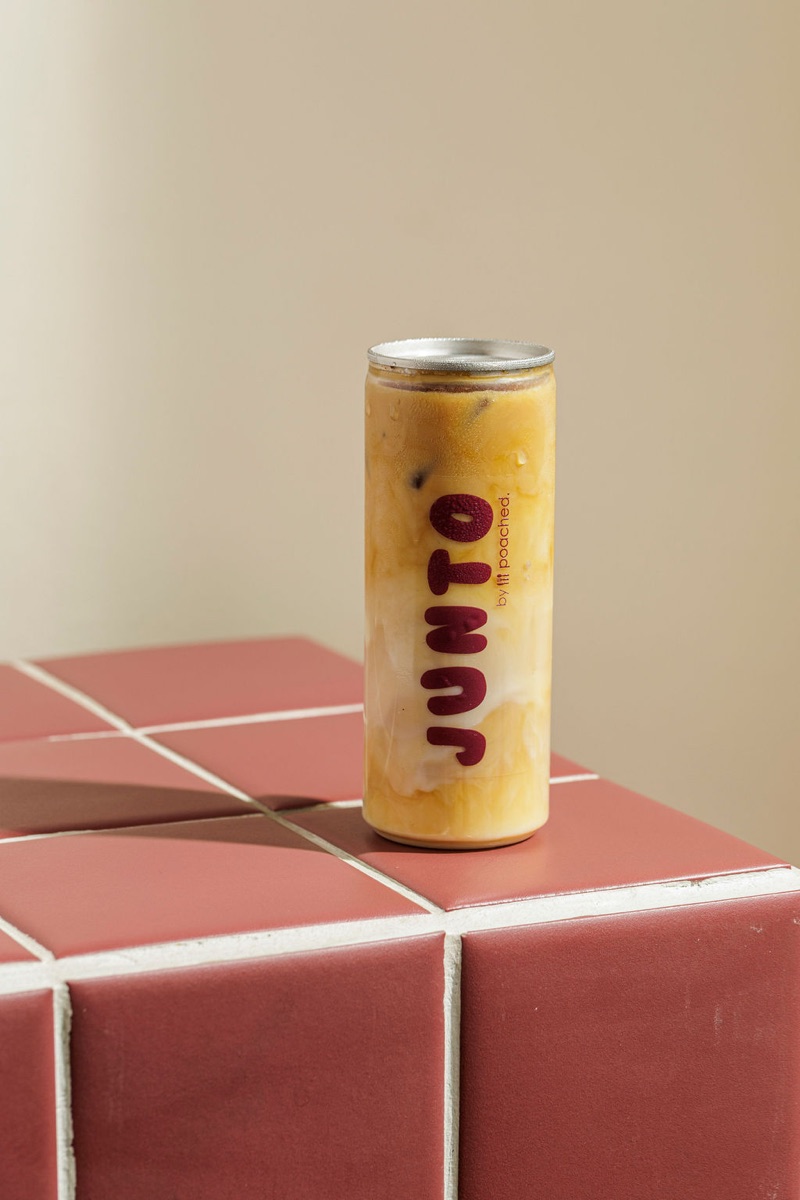 JUNTO iced coffee can on burgundy tile plinth, studio-lit.