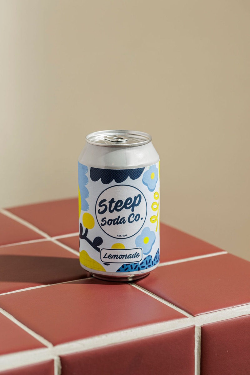 Steep Soda Co Lemonade can on the burgundy tile plinth.