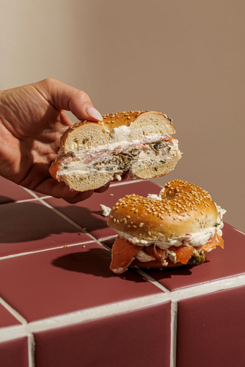A smoked salmon Cold Smoke bagel cross-section held above the burgundy tile plinth.