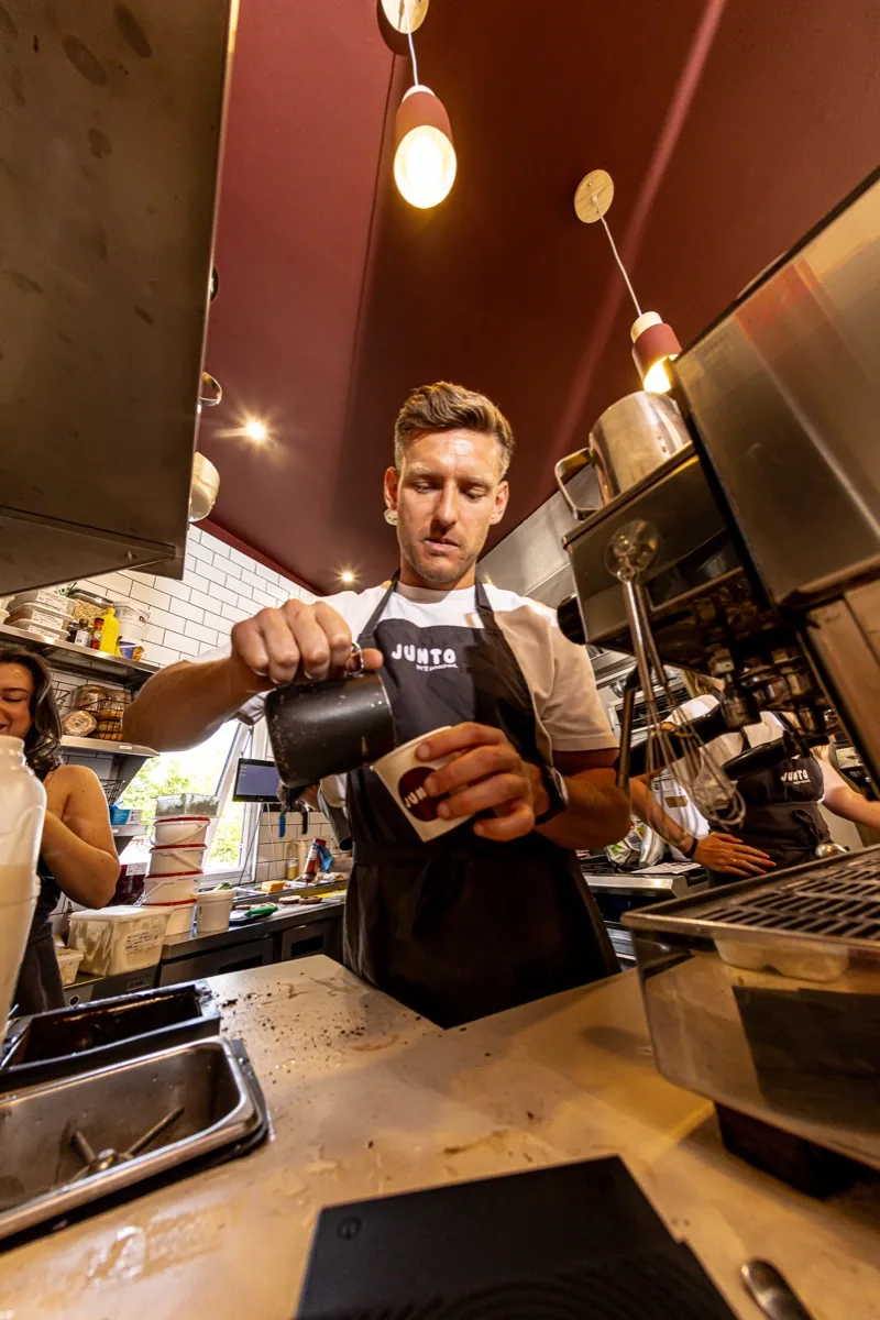 Barista in a JUNTO apron pouring steamed milk for a latte.